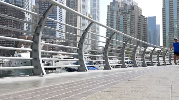 Lage hoekmening van atletische fitness man loopt in Dubai Marina joggen in de ochtend, slow-motion — Stockvideo