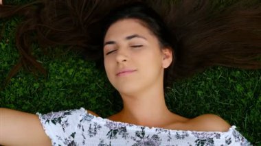 Genç güzel mutlu gülümseyen kız saç, 4 k yayılması ile çim üzerinde yalan
