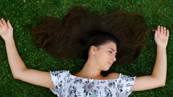 の髪の広がりと草の上に横たわる若い美しい幸せな笑顔の女の子 — ストック動画