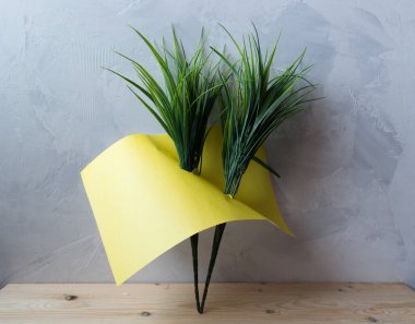 Gri arkaplanda parlak renkli kağıt bulunan yapay yeşil çimenler.