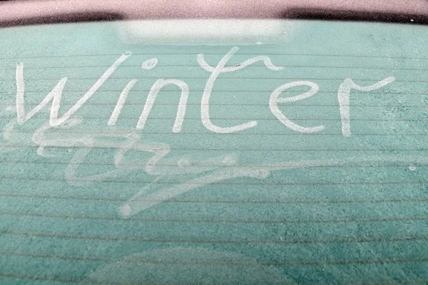 Слово зима написано на ветровом стекле замерзшей машины — стоковое фото