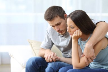 Sad couple comforting each other at home clipart