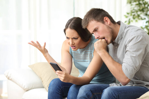 Angry couple with mobile phone at home