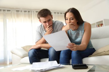 Worried couple reading a letter at home clipart