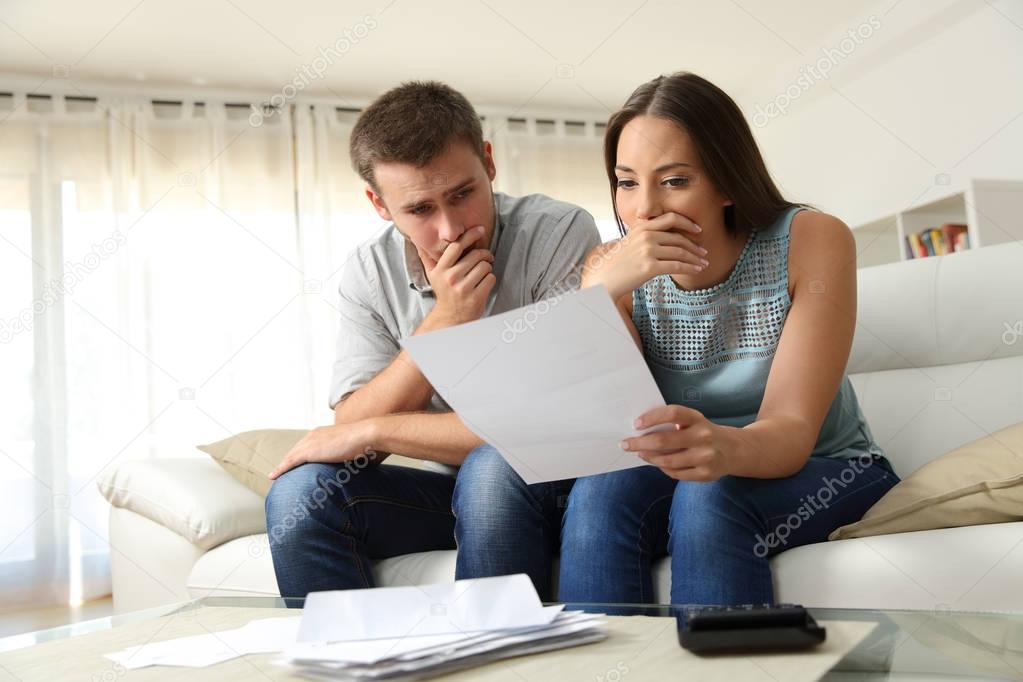 Worried couple reading a letter at home