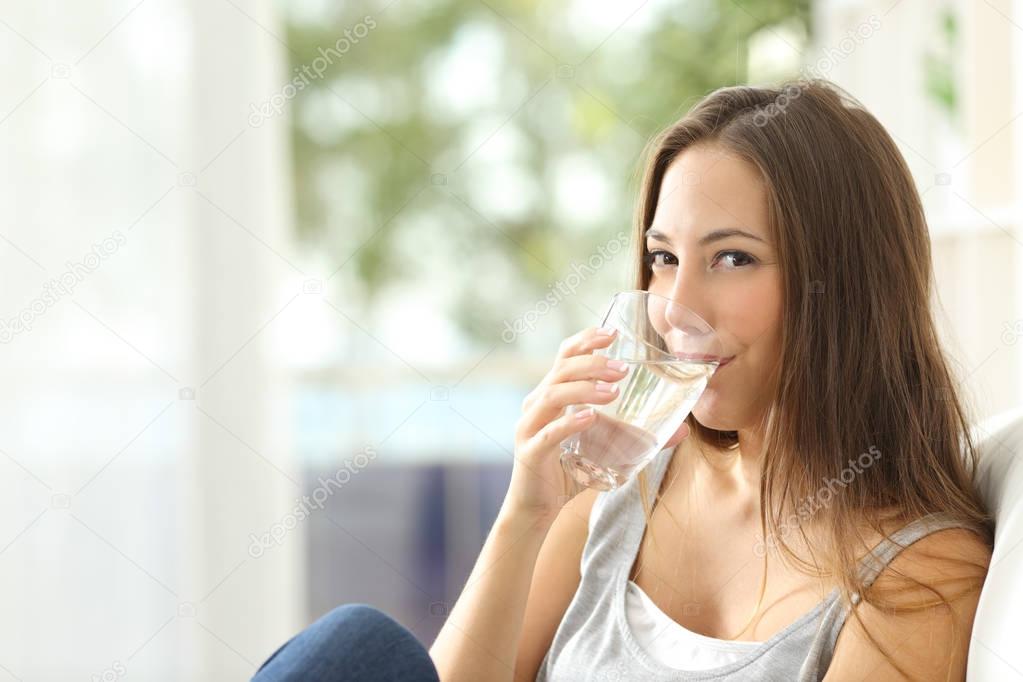 Woman drinking water at home and looking you