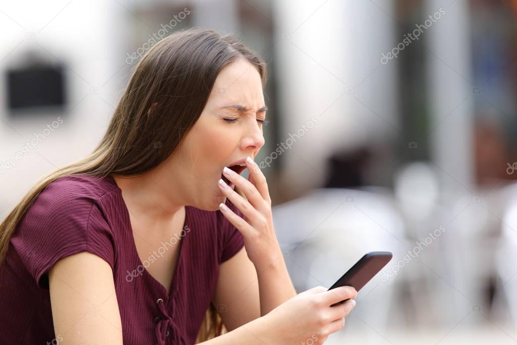 Bored woman yawning with a mobile phone