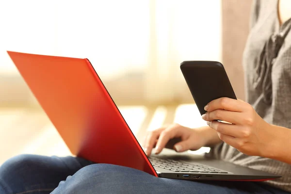 Mãos de menina usando um telefone e um laptop vermelho — Fotografia de Stock