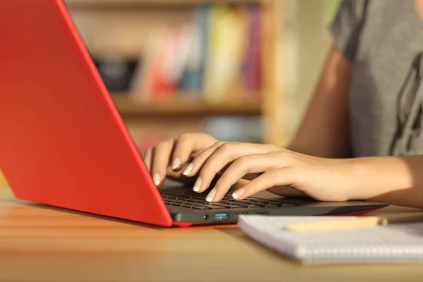 Student hands writing in a red laptop at home — Stock Photo, Image