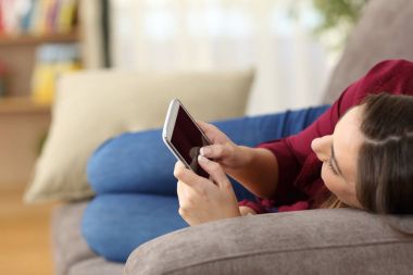 Kanepede yatan bir akıllı telefon kullanan kız