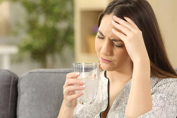Женщина страдает головной болью держа стакан — стоковое фото