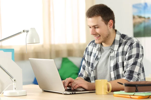 Щасливий студент пише в ноутбуці в своїй кімнаті — стокове фото