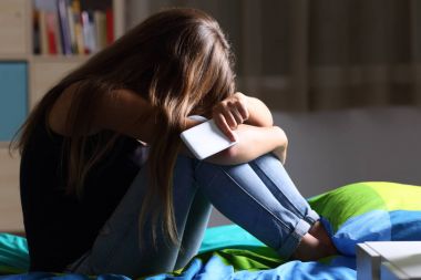Üzgün teen yatak odasında bir telefon ile