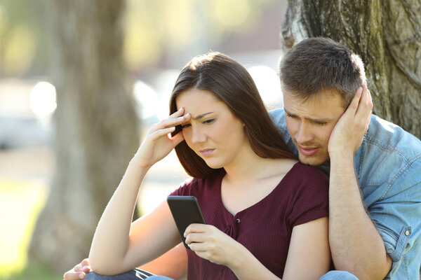 Worried couple using a smart phone outside
