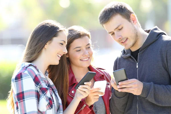 Tres amigos hablando sosteniendo sus teléfonos inteligentes —  Fotos de Stock