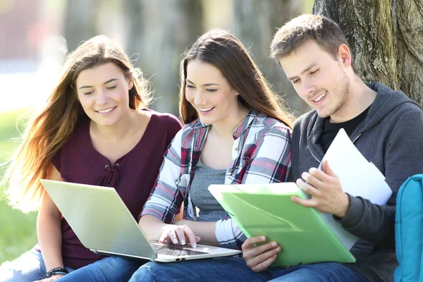 Drie gelukkige studenten die online studeren in een park — Stockfoto