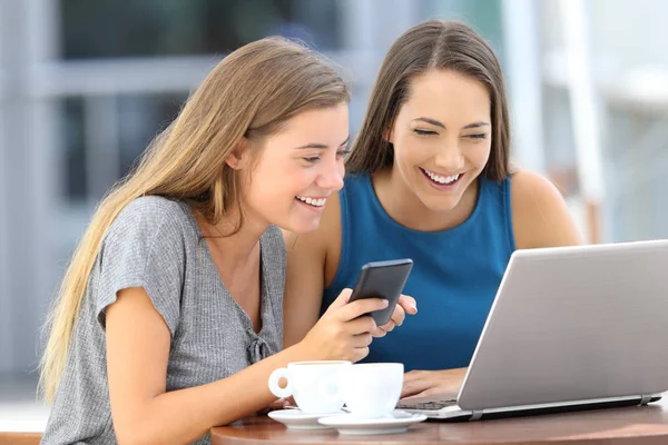 Glada vänner med hjälp av en bärbar dator och telefon i en bar — Stockfoto