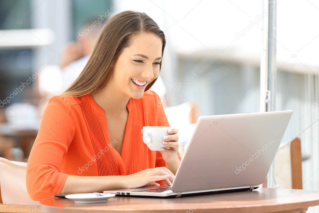 Happy woman browsing a laptop on line in a bar