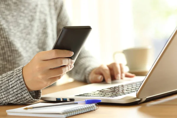 Mujer usando un teléfono y un portátil en una mesa — Foto de Stock