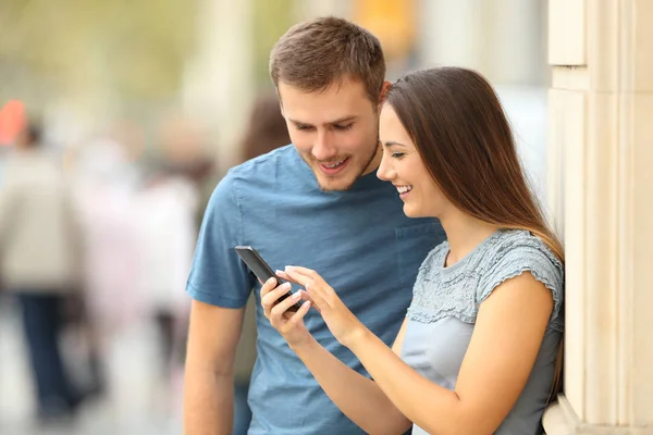 Couple checking content in a smart phone on the street — Stock Photo, Image