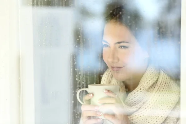 Chica mirando a través de una ventana sosteniendo el café en invierno —  Fotos de Stock