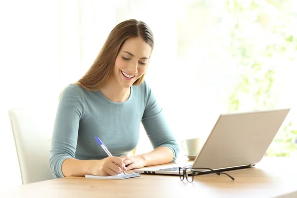 Vrouw schrijven van notities naast een laptop thuis — Stockfoto