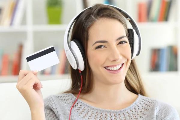 Chica escuchando música y mostrando la tarjeta de crédito en blanco —  Fotos de Stock