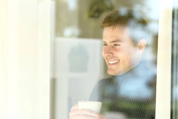 Man holding a coffee cup looking through a window — Stock Photo, Image