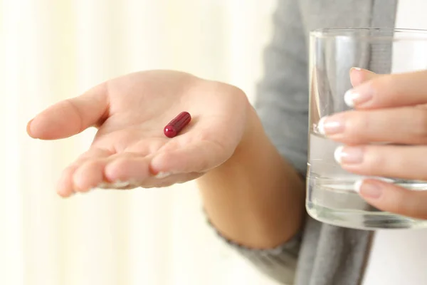 Mulher mão mostrando uma cápsula e um copo de água — Fotografia de Stock