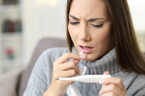 Mujer con fiebre buscando termómetro comiendo una pastilla — Foto de Stock