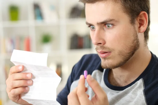 Шокированный человек читает брошюру перед тем, как принять таблетку — стоковое фото