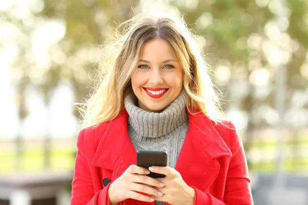 Krásná blondýnka při pohledu na fotoaparát drží chytrý telefon — Stock fotografie