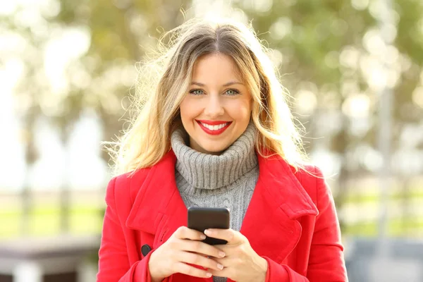 Hermosa rubia mirando la cámara sosteniendo un teléfono inteligente — Foto de Stock