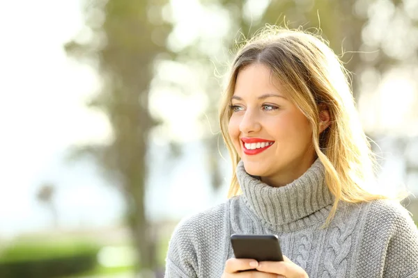 Щаслива дівчина дивиться і тримає телефон взимку — стокове фото