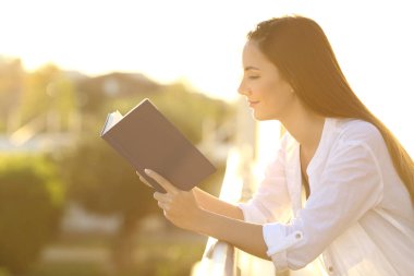 Kadın günbatımında bir balkon bir kitap okuma