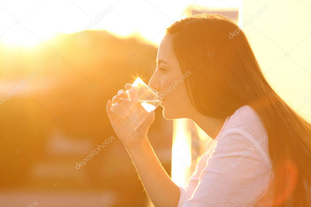 Woman drinking water from a glass at sunset