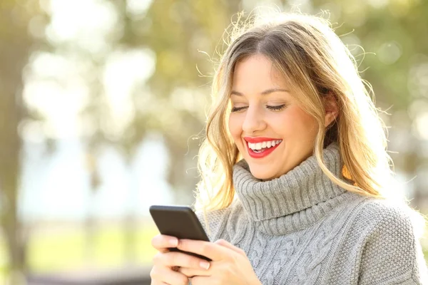 Счастливая женщина читает текст по телефону зимой — стоковое фото