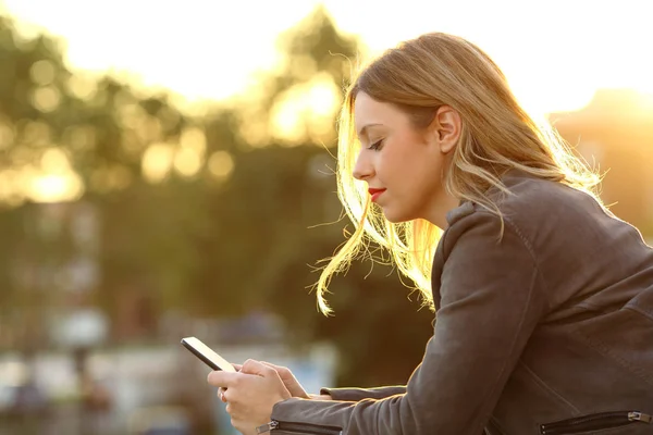 Kvinna läser texten i en smart telefon i solnedgången — Stockfoto