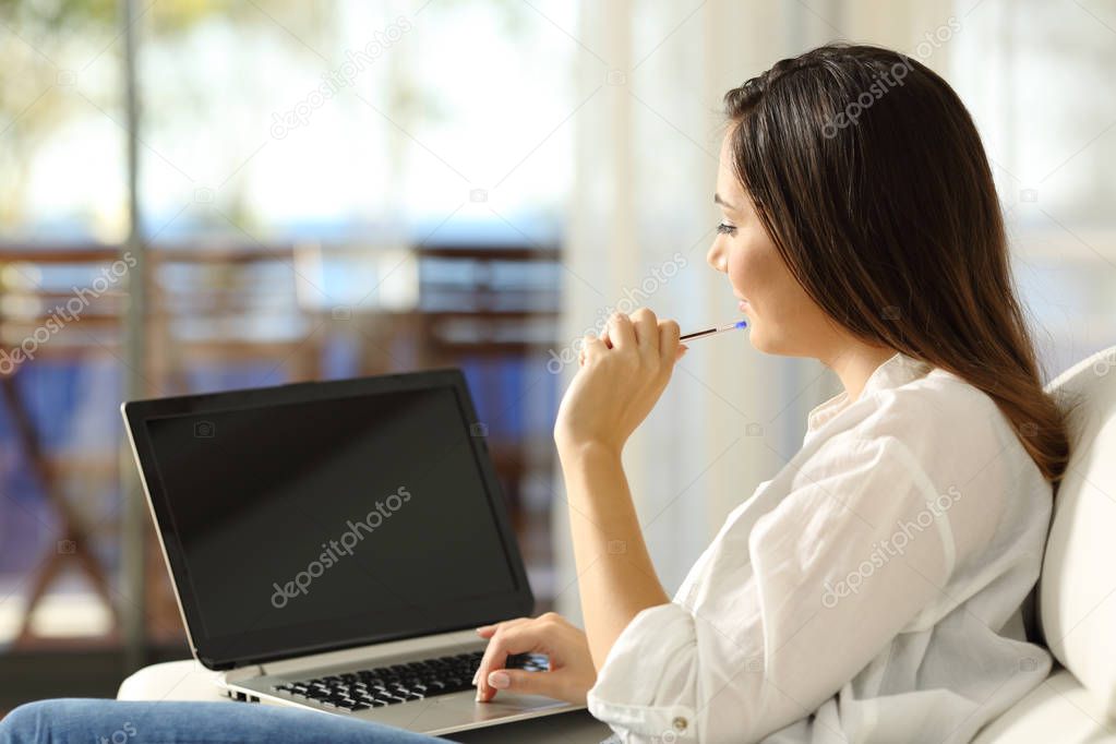 Woman thinking using a laptop with blank screen