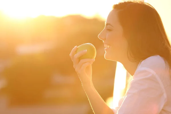 Profile of a woman eating an apple at sunset — Stock Photo, Image