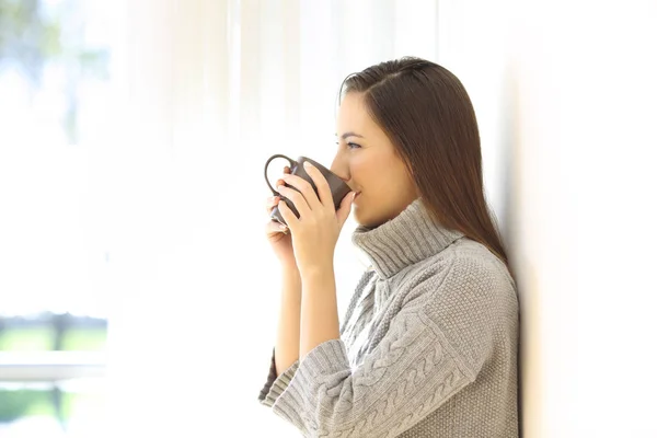 Жінка п'є каву, дивлячись через вікно — стокове фото