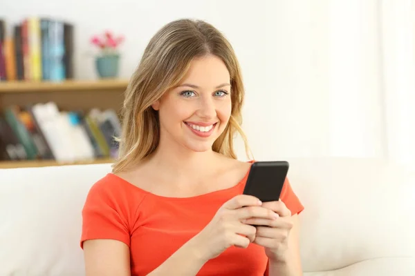 Chica mirando a la cámara sosteniendo un teléfono inteligente en casa — Foto de Stock