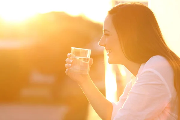 Ευτυχισμένη κυρία κρατώντας ένα ποτήρι νερό στο ηλιοβασίλεμα — Φωτογραφία Αρχείου