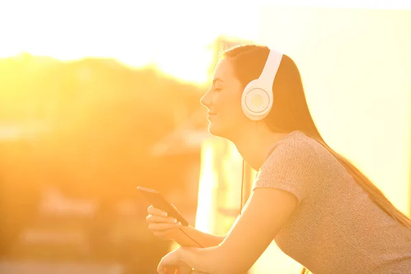 Relaxed girl listening to music outdoors at sunset