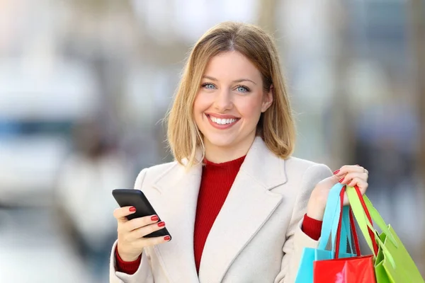 Shopper segurando sacos de compras e telefone olhando para a câmera — Fotografia de Stock