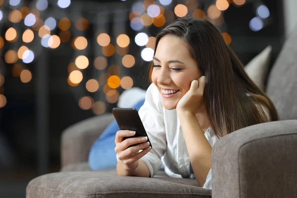 Pige ved hjælp af en smart telefon liggende på en sofa derhjemme - Stock-foto