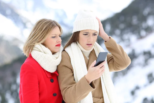 Confused friends with a smart phone in winter — Stock Photo, Image