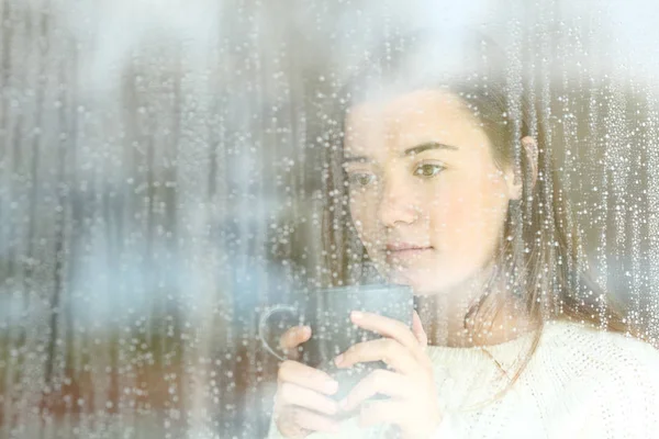 Adolescente ansioso olhando através de uma janela sozinho — Fotografia de Stock