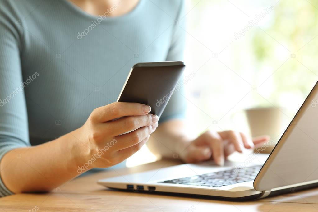 Girl hands using a smart phone and a laptop on a desk
