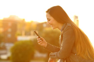 Günbatımında bir akıllı telefon kullanan bir kız profili